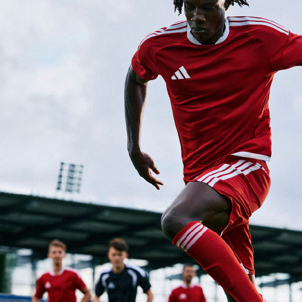 Soccer player in red uniform kicking the ball on a field with other players.